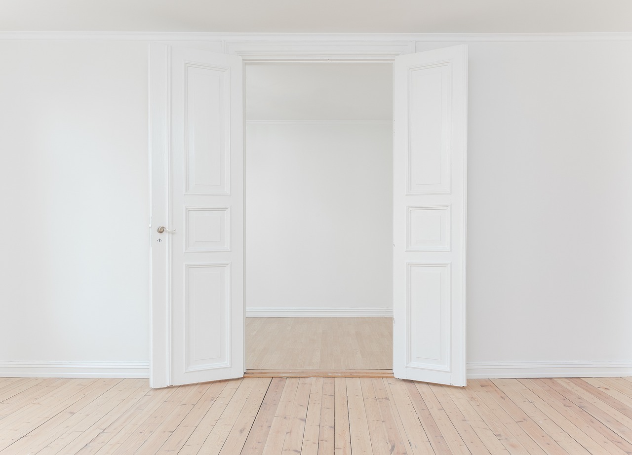 pièce vide en cours de rénovation, parquet clair et double porte blanche ouverte sur un couloir, sans mobilier