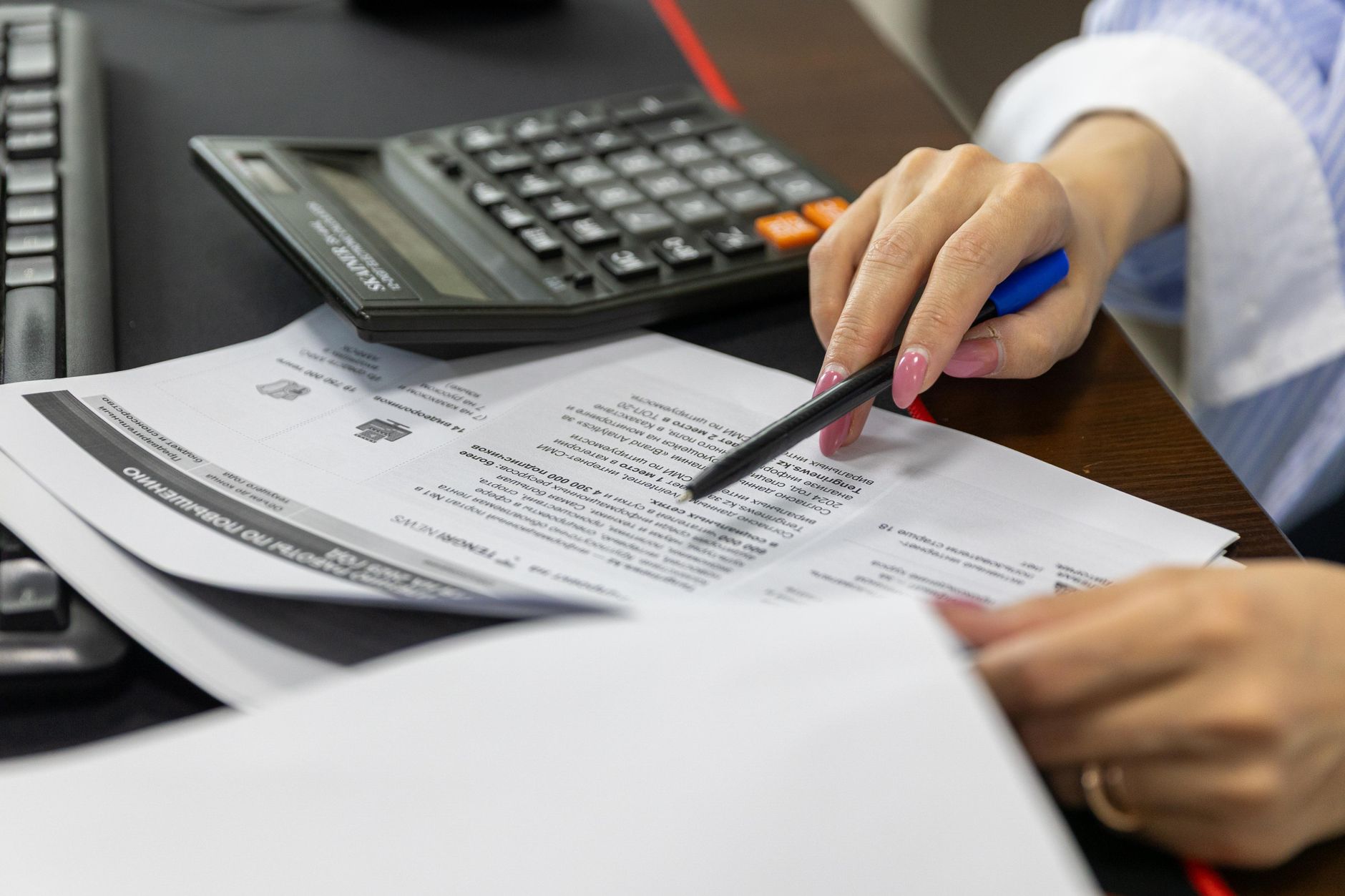 main tenant un stylo au-dessus d'un document chiffré, à côté d'une calculatrice, pendant la relecture d'un devis