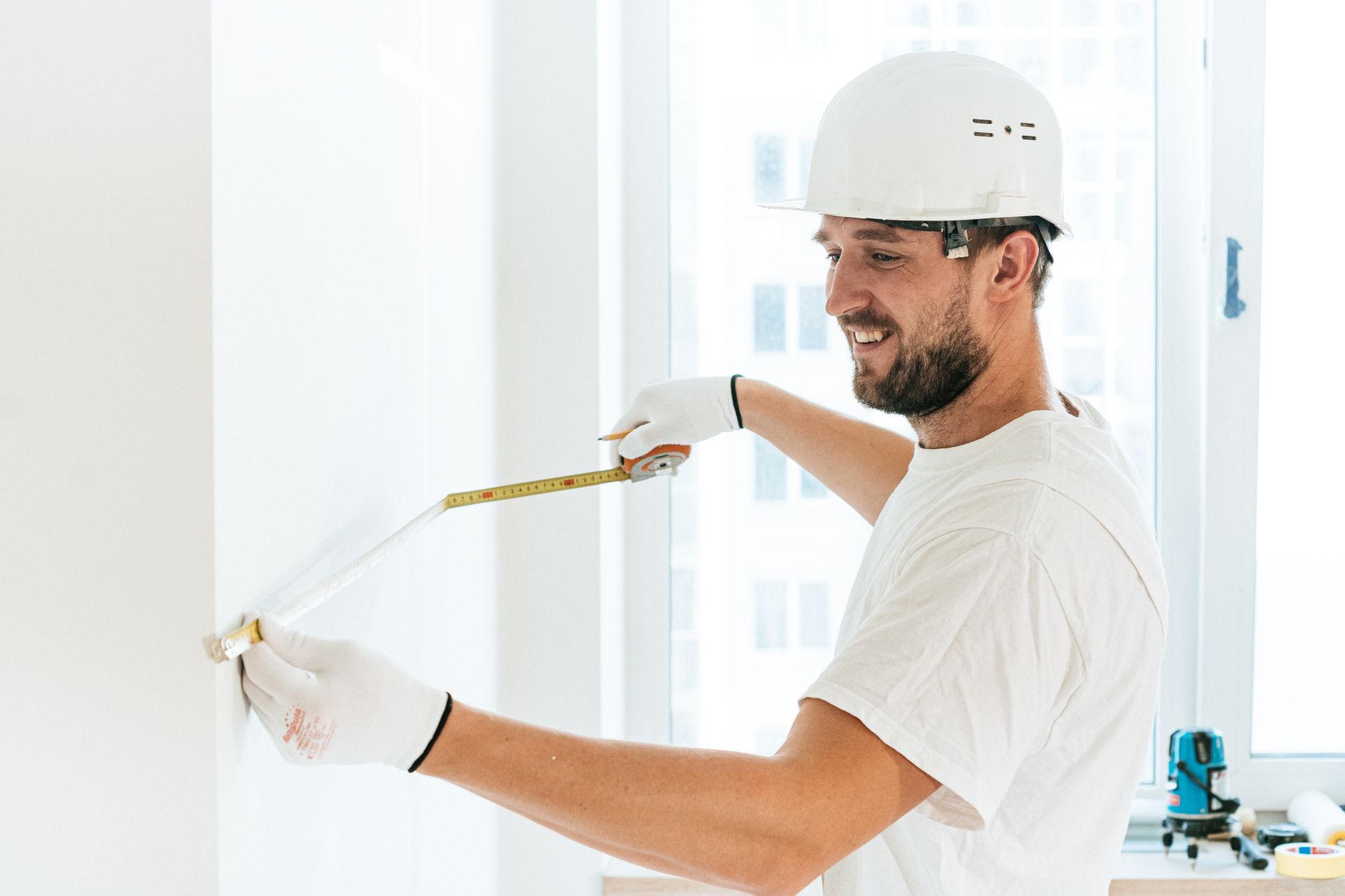 ouvrier en casque blanc et gants mesurant un mur intérieur au mètre ruban avant des travaux