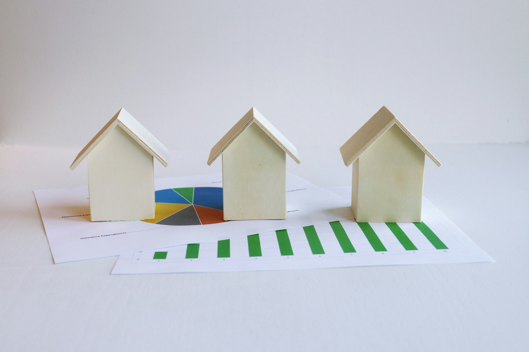 trois maisonnettes miniatures posées sur des graphiques et diagrammes imprimés, symbolisant le suivi de la valeur immobilière