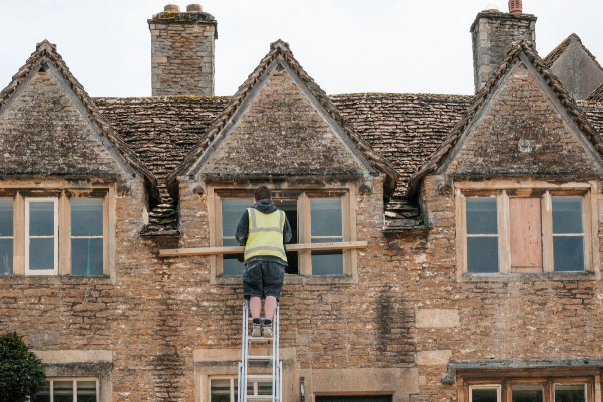 Artisan sur une échelle devant une maison ancienne en pierre en rénovation