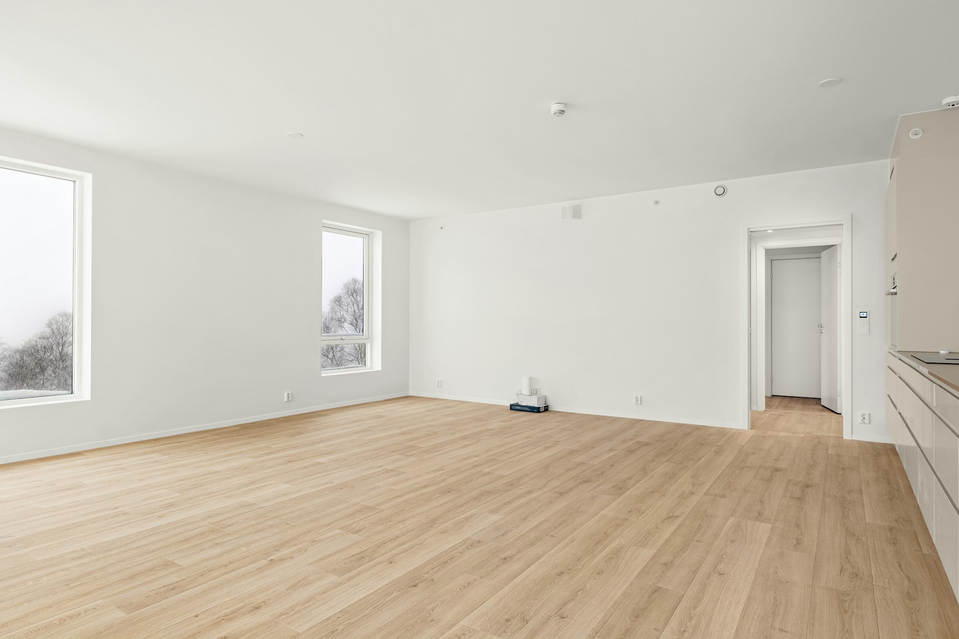 pièce vide aux murs blancs avec parquet clair et fenêtres, prête à être mesurée