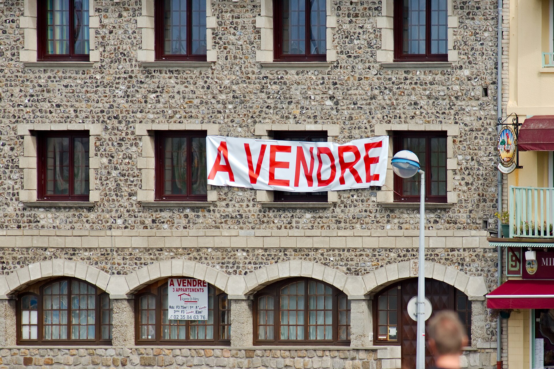 façade en silex d'un petit immeuble de Dieppe avec une banderole à vendre et une affiche d'agence annonçant trois appartements